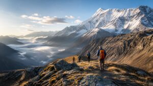Hikers on a high alpine ridge trail overlooking snow-covered peaks and a cloud-filled valley