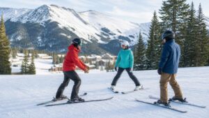Ski instructor teaching two adult beginners on a gentle snowy slope with mountains in the background